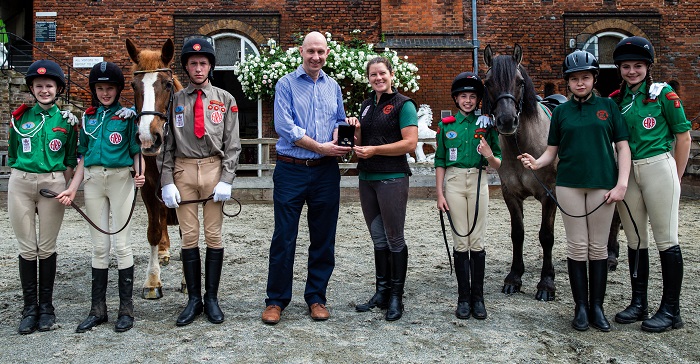 Maia Davies, Lola Doyle, Matthew Sheppard, Stephen Lee, managing director of Bradford Exchange, Theresa Barrett, stable manager of The Horse Rangers Association, Caitlin Aldous, Hollie Driver, and Abi Evans pose during the launch of the gold quarter sovereign to feature the portrait of the Queen on horseback, released by The Bradford Exchange at The Horse Rangers Association, Royal Mews, Surrey. Photo credit: Steven Paston/Press Association.